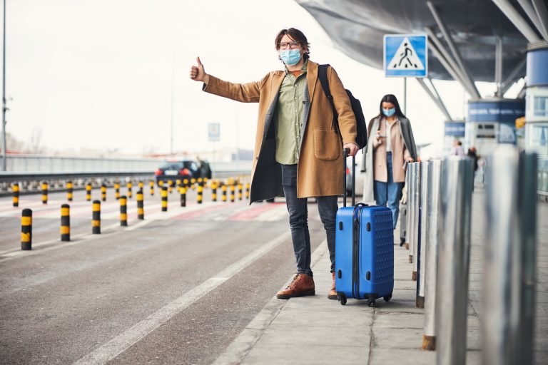Stylish young man in medical mask catching taxi at airport