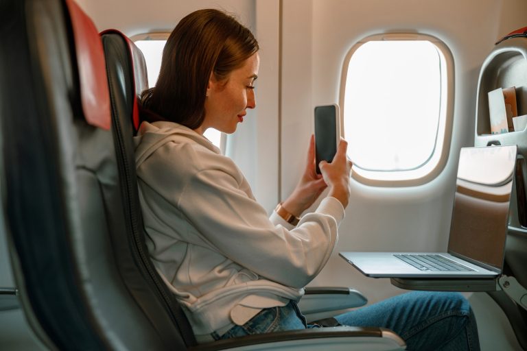 Young woman taking picture with smartphone in airplane